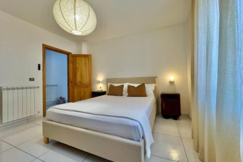 A bedroom with a large bed, a wooden door, a radiator, and a ceiling light fixture.
