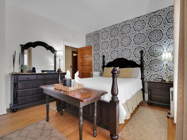 Une chambre à coucher avec un lit en bois, une commode, une table de chevet, un miroir et un papier peint à motifs.