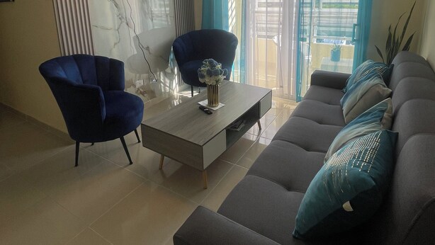 A living room with a sofa, two armchairs, a coffee table, a TV mounted on the wall, and a chandelier. - POSADA DEL CARIBE (Santo Domingo Este)