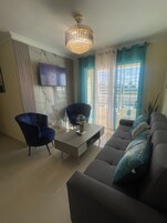 Una sala de estar con sofá, dos sillones, una mesa de centro, televisor montado en la pared y candelabro.