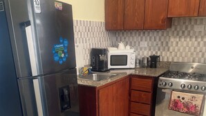 A kitchen with a stainless steel refrigerator, a microwave, a gas stove, wooden cabinets, and a tiled backsplash. - POSADA DEL CARIBE (Santo Domingo Este)