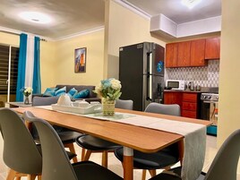Un espacio habitable compacto con comedor, cocina y un sofá con cojines azules.