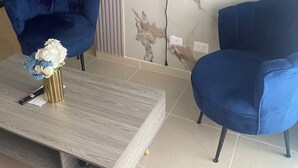 A modern living room with two blue armchairs, a coffee table with a vase of flowers, and a flat-screen TV mounted on a marble wall. - POSADA DEL CARIBE (Santo Domingo Este)