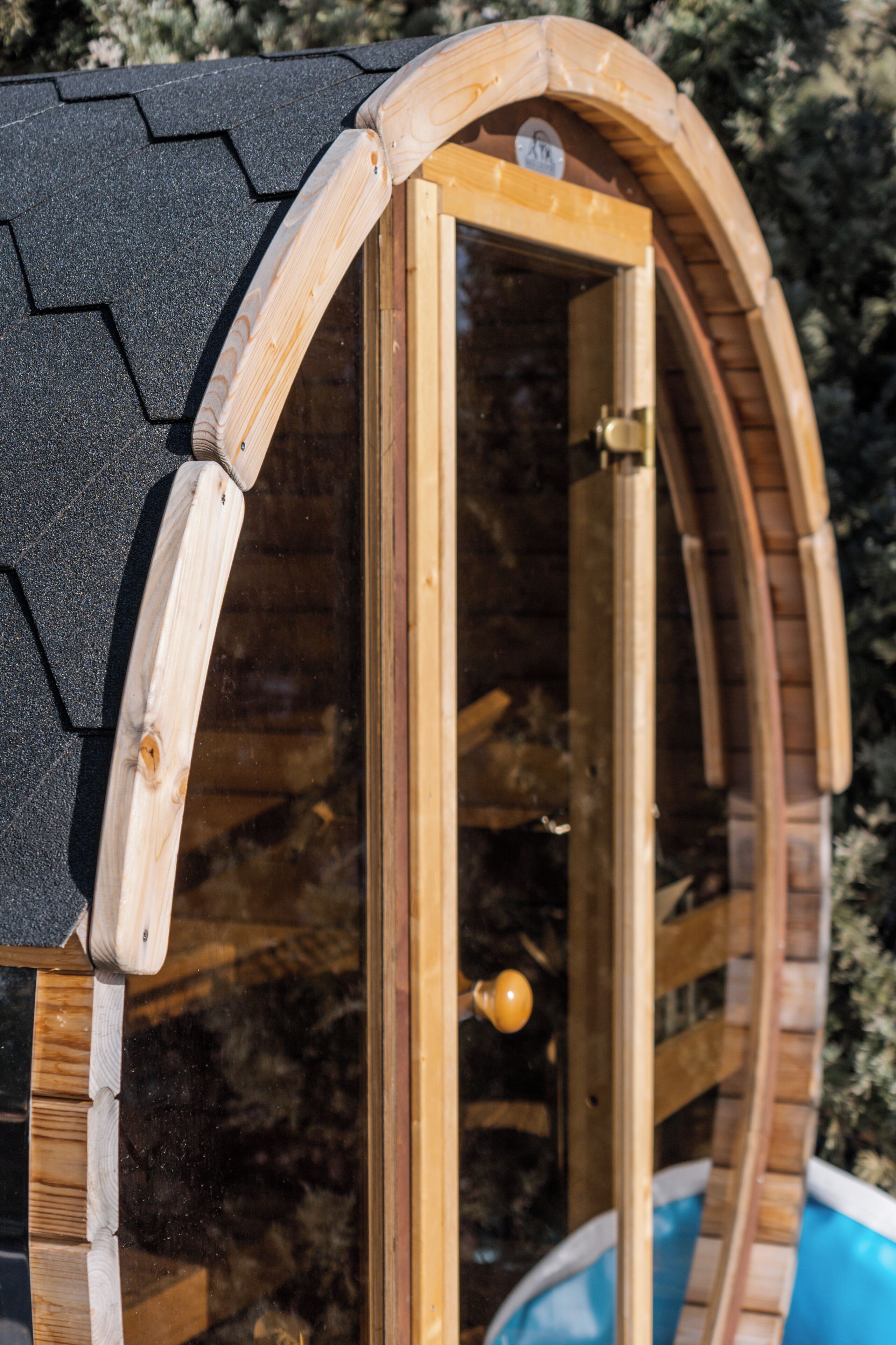 Une structure en bois dotée d’un toit incurvé et d’une porte en verre, qui ressemble probablement à une serre ou à un abri de jardin.