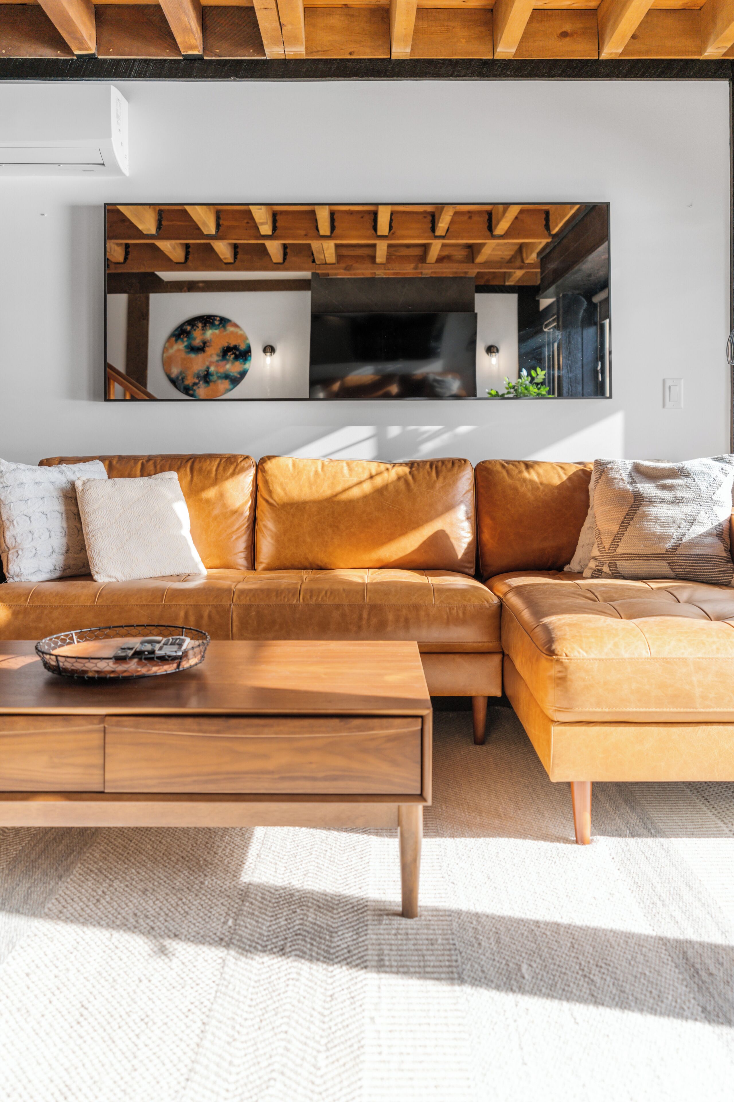 Un salon moderne avec un canapé d’angle en cuir marron, une table basse en bois et un grand tableau abstrait accroché au mur.