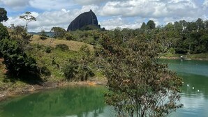 A natural landscape with a large rock formation, a body of water, and surrounding greenery. - SINPRISA "NOT RUSH "PRECIOUS CABIN! withJacuzzi, stone view, direct access to the reservoir (GUATAPE)