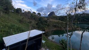 A modern building with a metal roof, situated on a grassy hill overlooking a calm lake. - SINPRISA "NOT RUSH "PRECIOUS CABIN! withJacuzzi, stone view, direct access to the reservoir (GUATAPE)