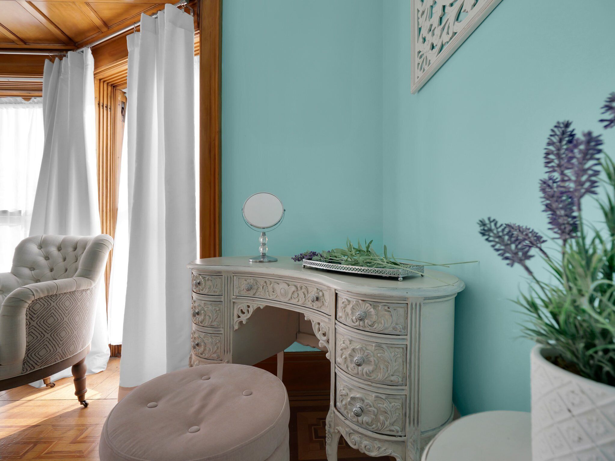A room with a white ornate dresser, a round mirror, and a potted plant.
