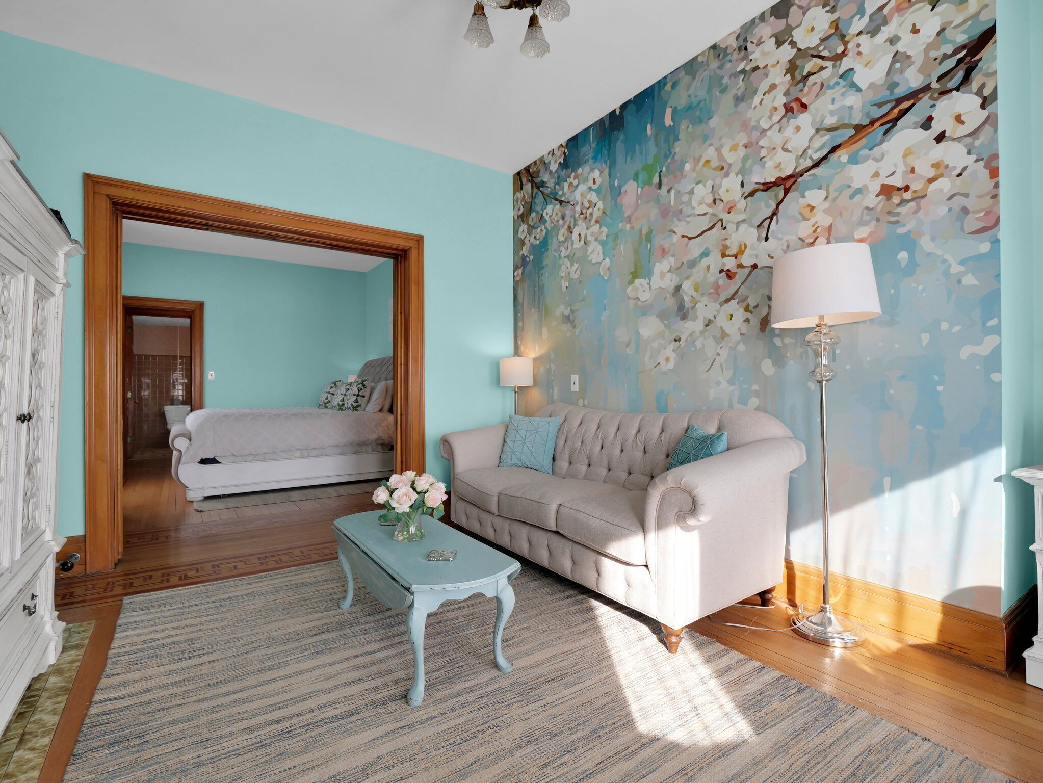 A room with a bed, a sofa, a coffee table, a painting, and a lamp.