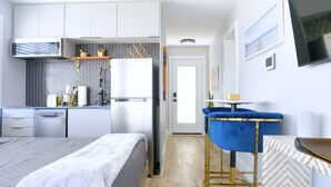Una cocina moderna con armarios blancos, microondas y refrigerador. Hay una silla azul con marco dorado cerca de una mesita.
