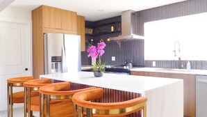 Een moderne keuken met een centraal kookeiland, barstoelen, een koelkast en een backsplash met een herringbone-patroon.