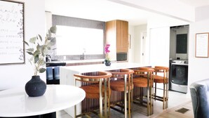 Een moderne keuken met een centraal eiland, barstoelen en een eettafel.