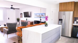 Een moderne keuken met een centraal eiland, een eethoek met stoelen, een koelkast en een plafondventilator.
