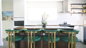 A modern kitchen with a central island, bar stools, a potted plant, and a window with a view.