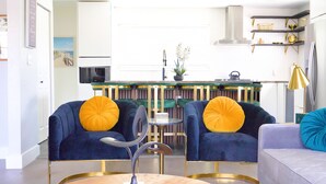 A modern living room with two blue armchairs, a small round table, and a sofa with a blue cushion.