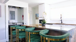 A modern kitchen with a marble countertop, green bar stools, a sink, and a fire extinguisher.
