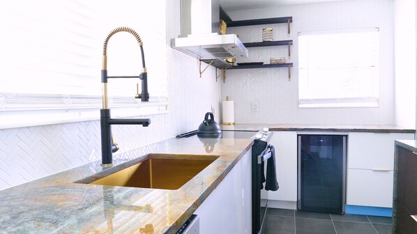 Una cocina moderna con una encimera de granito grande, un lavaplatos empotrado y un lavavajillas compacto.