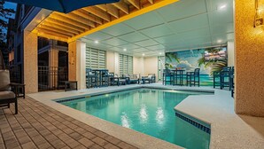 Una piscina interior con sillones de descanso y sombrillas, rodeada de paredes de azulejos y un mural de una playa tropical.