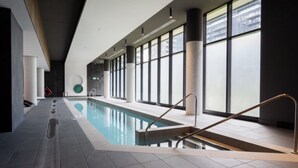 A modern indoor swimming pool with clear glass walls, a tiled floor, and a minimalist design. - Mid-century getaway (Brossard)