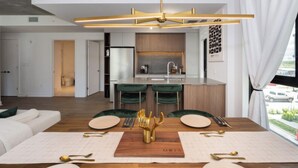A modern kitchen with a central island, bar stools, and a dining area with a wooden table set for two. - Mid-century getaway (Brossard)