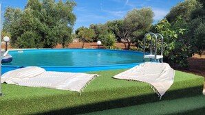 A swimming pool with a ladder, two towels on artificial grass, and trees in the background.