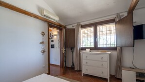 A bedroom with a bed, a dresser, a window with curtains, and an air conditioning unit.