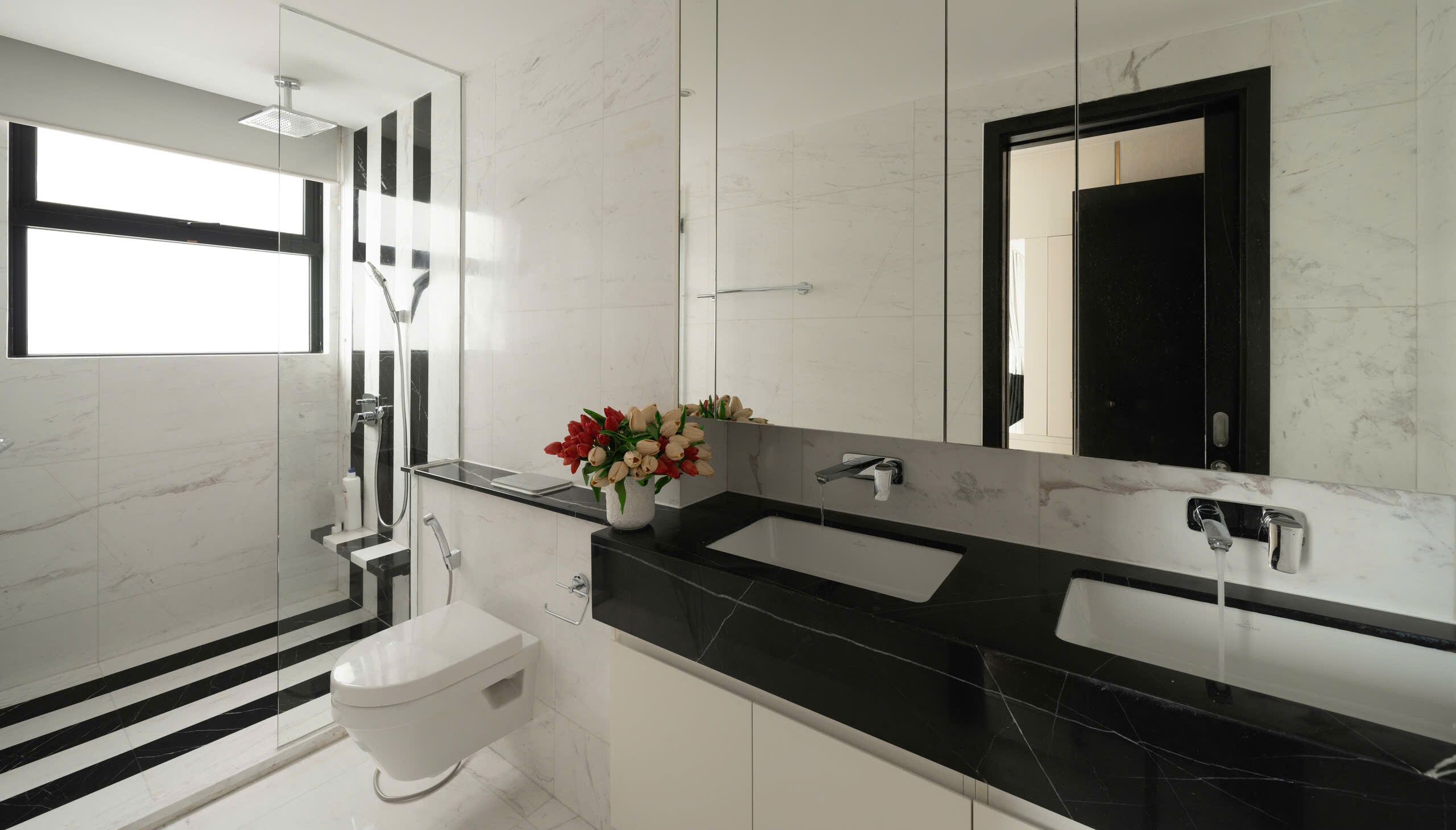 A modern bathroom with a glass shower enclosure, a toilet, two sinks, and a large mirror.