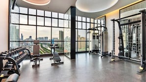 A modern gym with large windows, various exercise equipment, and a city view.