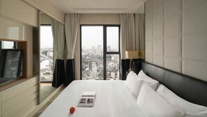 A hotel room with a large bed, a TV, a city view, and a lamp.