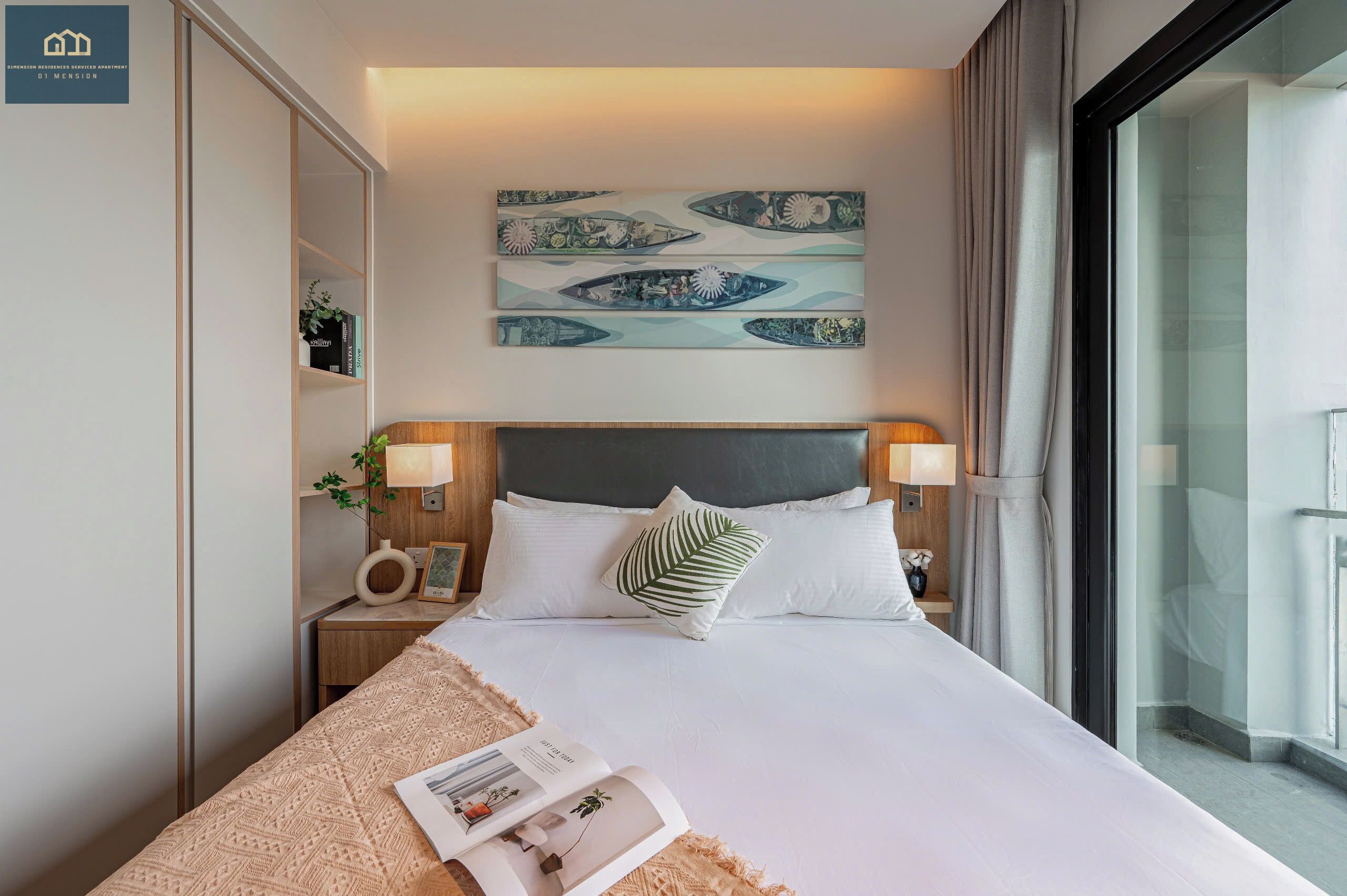 A modern hotel room with a large bed, a bedside table with a lamp, a wall-mounted artwork, and a view through a glass door.