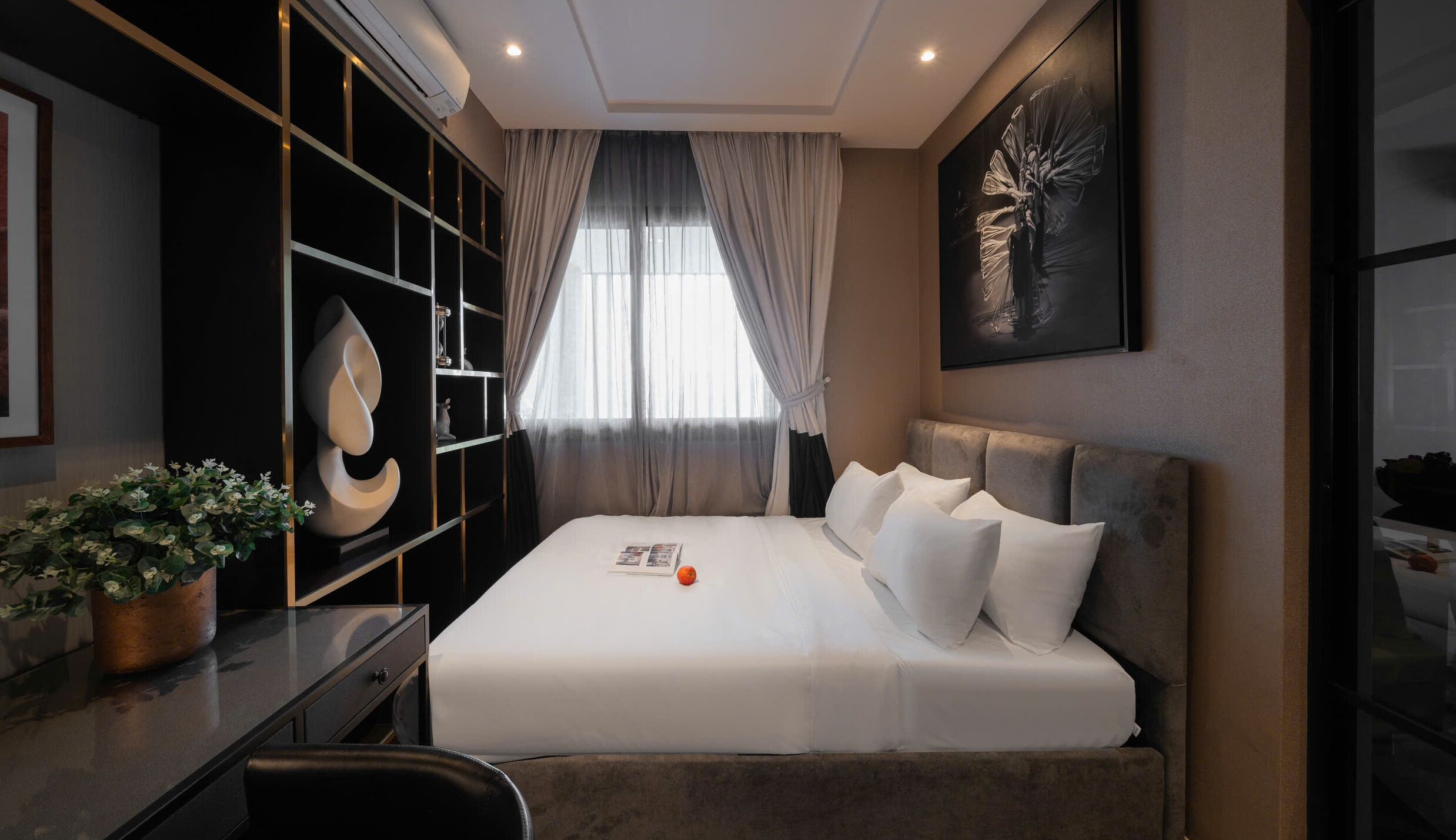 A modern hotel room with a large bed, a desk, and a potted plant.