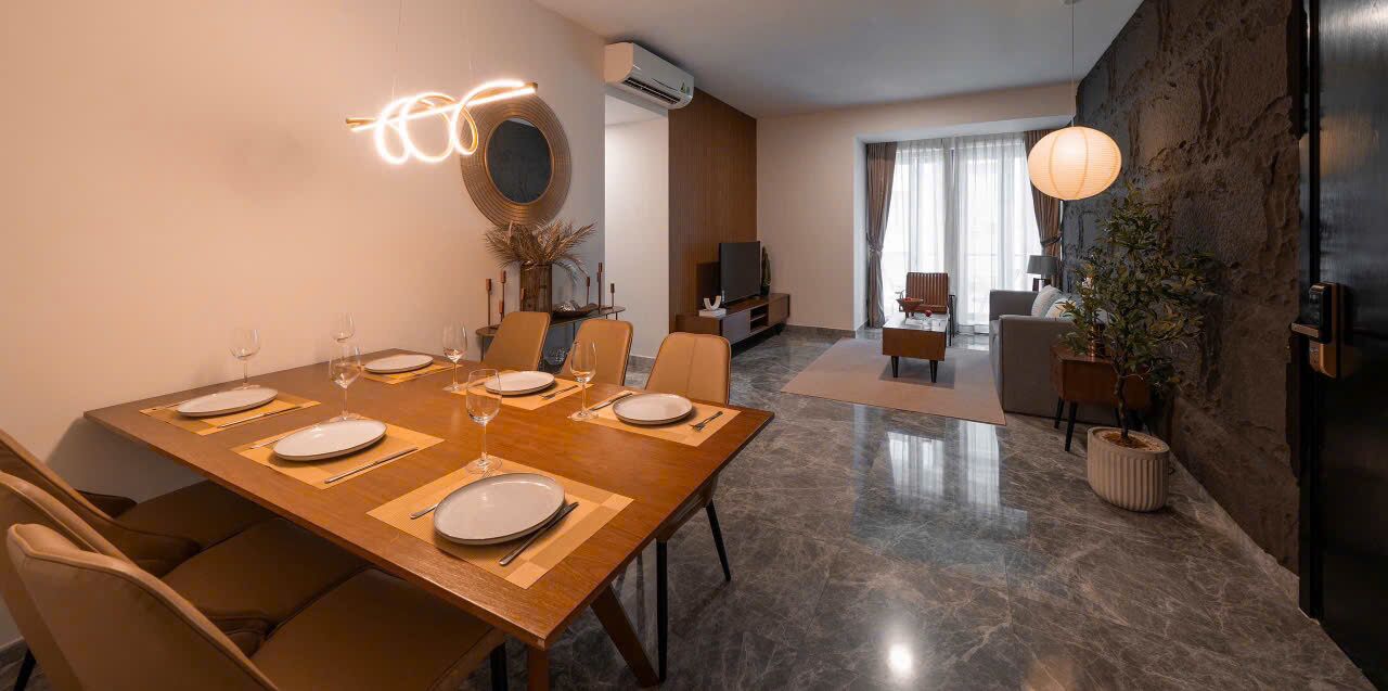 Een moderne eethoek met een houten tafel gedekt voor zes personen, een televisie op de achtergrond en een accentmuur van steen.