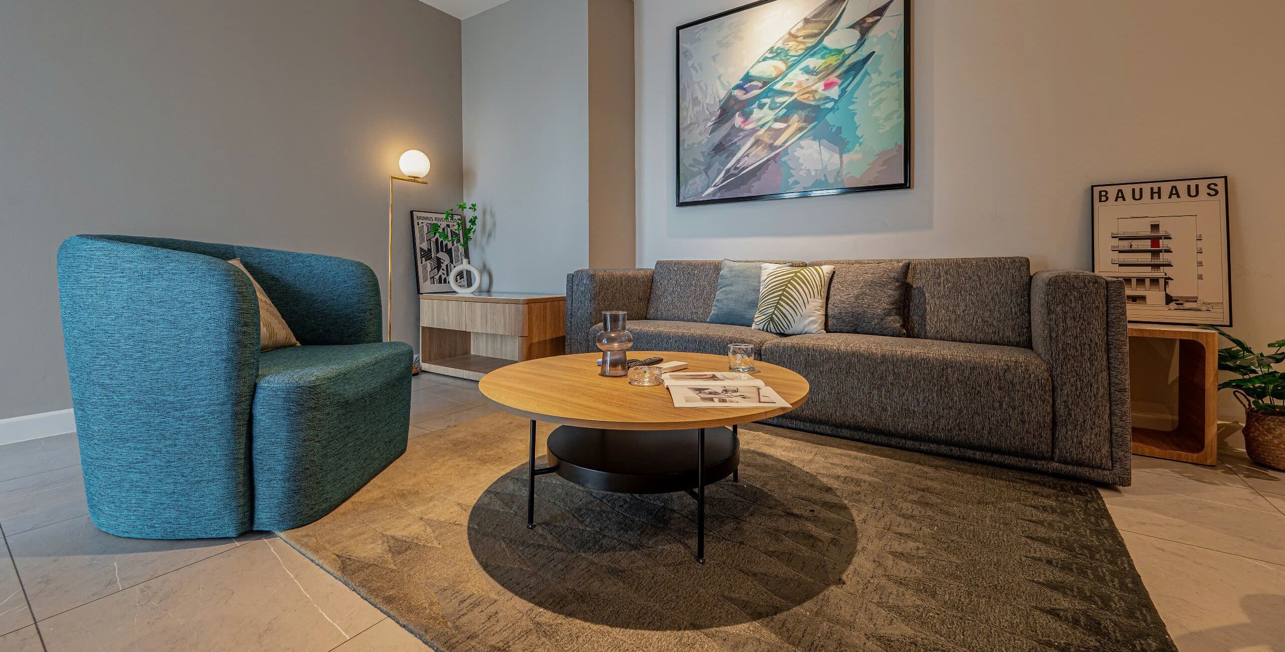Een moderne woonkamer met een blauwe fauteuil, een grijze bank en een ronde salontafel.