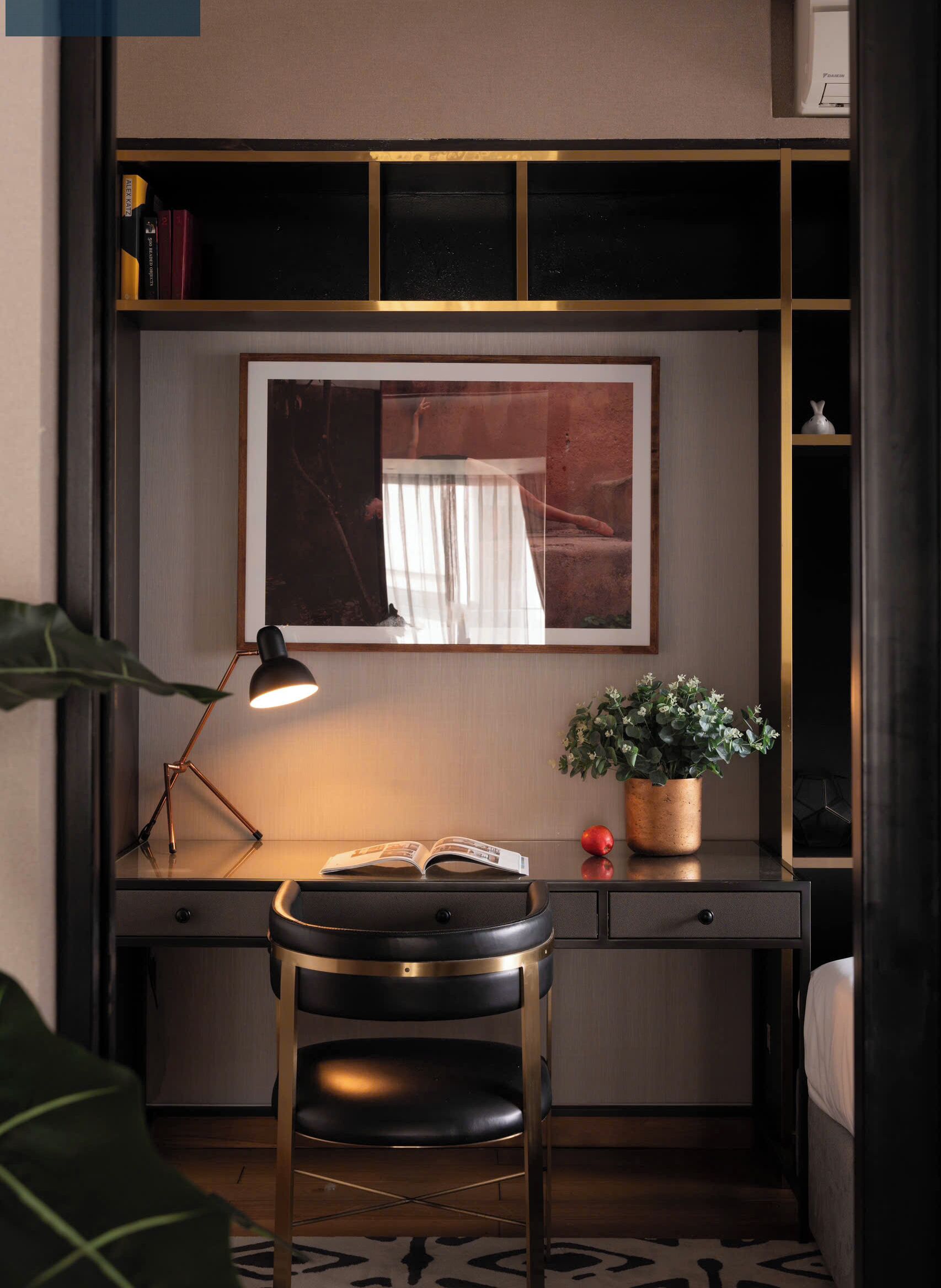 A modern study room with a desk, a chair, a desk lamp, a framed picture, a potted plant, and a bookshelf.