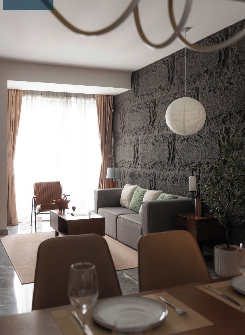 Un salon moderne avec un canapé gris, une table à manger avec des chaises et une grande fenêtre avec des rideaux.