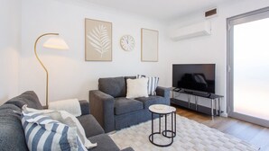 A modern living room with a grey sofa, a round coffee table, a floor lamp, a flat-screen TV, and a large window. - Little Fig Retreat - 5 mins to Fremantle (Samson)