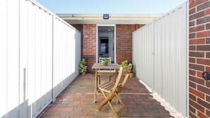 A small patio area with a brick wall, white metal fencing, a wooden table with chairs, and potted plants. - Little Fig Retreat - 5 mins to Fremantle (Samson)