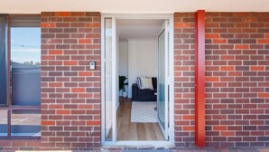 A doorway leading to a room with a dark-colored sofa and a small table, a potted plant, and a checkered rug on the floor. - Little Fig Retreat - 5 mins to Fremantle (Samson)