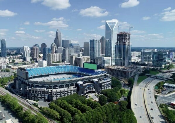 A cityscape with a large stadium surrounded by modern high-rise buildings, including a distinctive skyscraper under construction. - 3-bedroom bungalow in charming Charlotte (Charlotte)