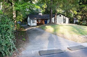 A small, single-story house with a front door and a garage, surrounded by trees and a sloped driveway. - 3-bedroom bungalow in charming Charlotte (Charlotte)