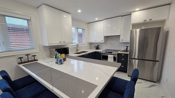 Una cocina moderna con armarios blancos, una isla central con taburetes y un refrigerador de acero inoxidable, además de un microondas.