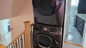 Cocina compacta con lavadora y secadora integradas, una escalera de madera y vistas al área de estar contigua.