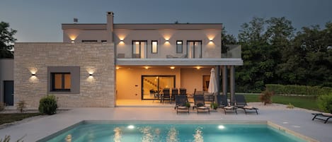 A modern house with a swimming pool, outdoor seating, and a stone facade.