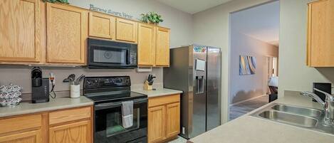 A modern kitchen with wooden cabinets, a black stove, a microwave, a refrigerator, and a sink.