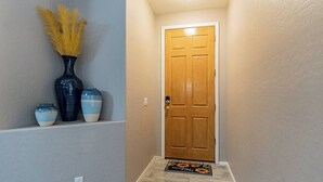 A hallway with a wooden door, a doormat, and decorative vases on a shelf.