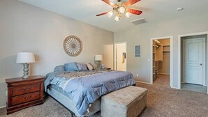 A bedroom with a bed, bedside tables, a ceiling fan, and a door leading to a hallway.