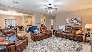 A spacious living room with leather sofas, a chandelier, and a ceiling fan.