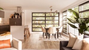 Ein modernes Wohnzimmer mit Essbereich, großen Fenstern und einer Küche im Hintergrund.
