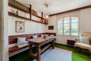 Una habitación con un banco de madera, una mesa, una lámpara colgante y una ventana con vistas a la vegetación.