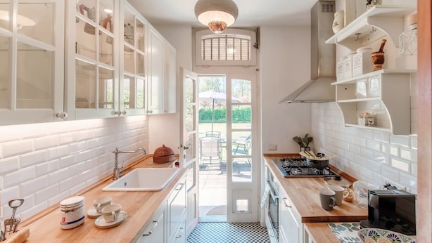 A kitchen with white cabinets, a checkered floor, a sink, a stove, and a dining area visible through a door. - Country House Montorfano (Capiago Intimiano)